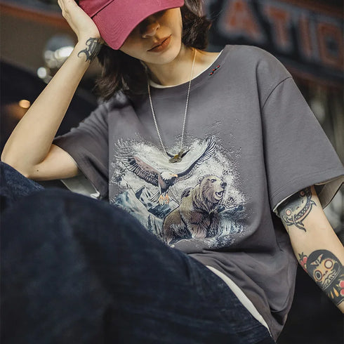Person wearing a gray t-shirt with a graphic design of a bear and eagle, sitting in a casual setting.
